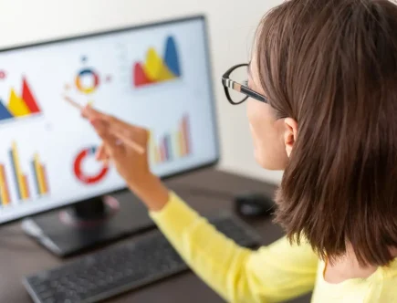 A imagem mostra uma mulher analisando gráficos em um computador, destacando a importância das métricas no marketing e como elas podem influenciar sua estratégia.
